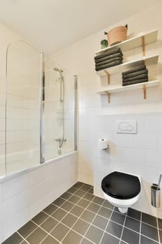 a bathroom with black and white tiles on the floor, tub, toilet, shower stall and shelves above it