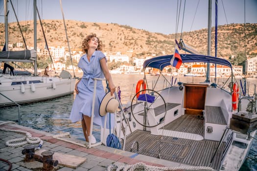 Woman yacht sea. A young happy woman in a blue dress and hat stands near the seaport with luxury yachts. Travel and vacation concept.