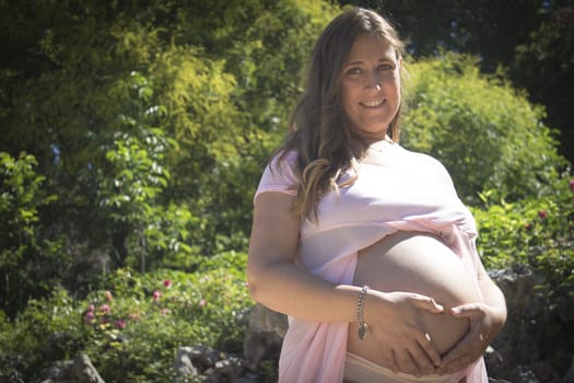 Pregnant woman with pink dress in a park. Sunny day