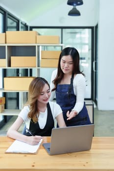 Starting small business two entrepreneur of independent Asian woman smiling using computer laptop with cheerful success of online marketing package box items and SME delivery concept.