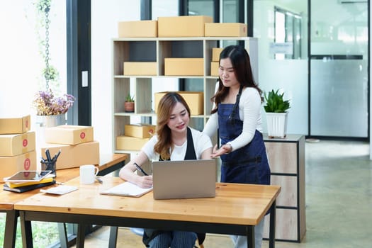 Starting small business two entrepreneur of independent Asian woman smiling using computer laptop with cheerful success of online marketing package box items and SME delivery concept.