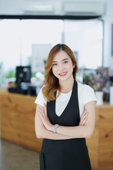 Starting and opening a small business, a young Asian woman showing a smiling face in an apron standing in front of a coffee shop bar counter. Business Owner, Restaurant, Barista, Cafe, Online SME.