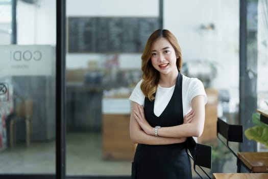 Starting and opening a small business, a young Asian woman showing a smiling face in an apron standing in front of a coffee shop bar counter. Business Owner, Restaurant, Barista, Cafe, Online SME.