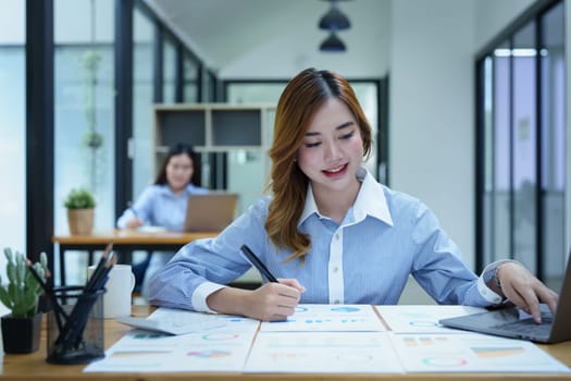 Portrait of a thoughtful Asian businesswoman looking at financial statements and making marketing plans using a computer on her desk.