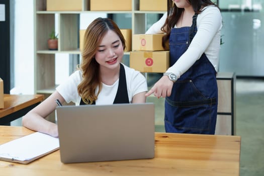 Starting small business two entrepreneur of independent Asian woman smiling using computer laptop with cheerful success of online marketing package box items and SME delivery concept.