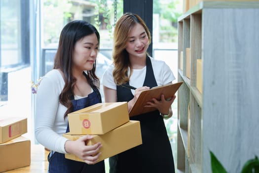 Starting small business two entrepreneur of independent Asian woman smiling using computer laptop with cheerful success of online marketing package box items and SME delivery concept.