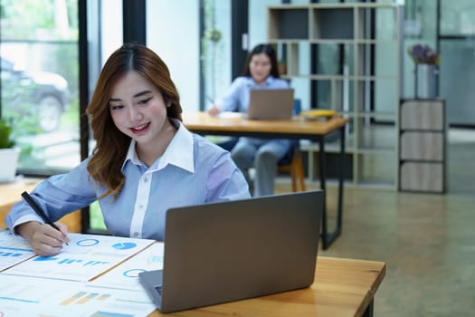 Portrait of a thoughtful Asian businesswoman looking at financial statements and making marketing plans using a computer on her desk.