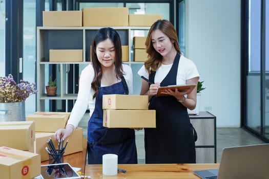 Starting small business two entrepreneur of independent Asian woman smiling using computer laptop with cheerful success of online marketing package box items and SME delivery concept.