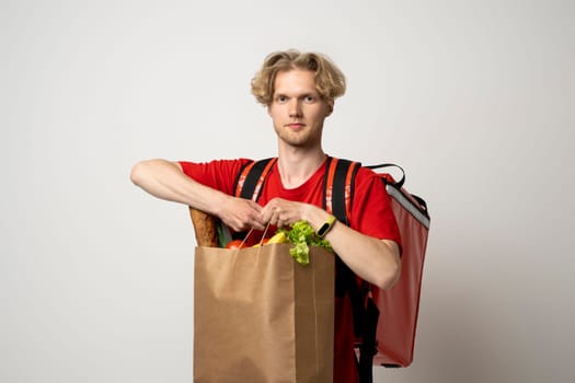 Portrait of smiling cheerful handsome young delivery man holding grocery shopping bag isolated on white background