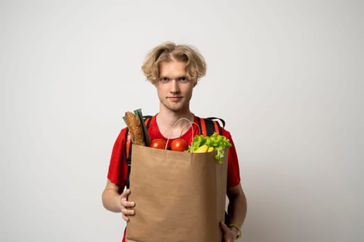 Delivery man employee in red t-shirt uniform hold craft paper packet with food isolated on white background studio