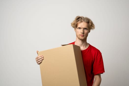Young courier man in red uniform carrying a box, parcel. Delivery service, post