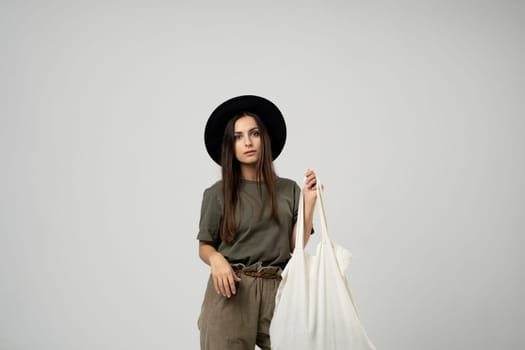 Happy smiling brunette woman in black hat with white cotton eco bag on her shoulder. Girl holding textile grocery bag with vegetables. Zero waste concept