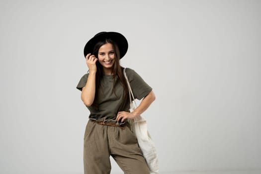 Happy smiling brunette woman in black hat with white cotton eco bag on her shoulder. Girl holding textile grocery bag with vegetables. Zero waste concept