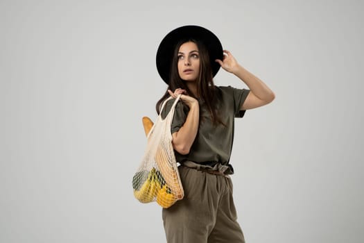 A modern stylish woman with a mesh shopping bag with vegetables against the background of the studio. The concept of healthy nutrition, vegetarianism and ecology. Refusal of plastic bags