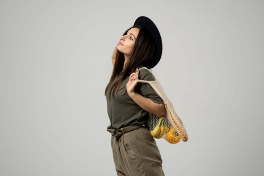 Zero waste concept. A young girl holds on her shoulder a textile mesh eco bag with a groceries. The girl smiles, wearing a beige t-shirt and hat. Refusal of plastic bags