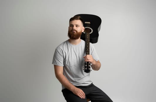Bearded man in grey t-shirt with a acoustic guitare. Music performer musician. Mature charismatic male guitarist with a string instrument