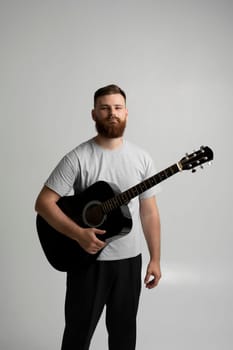 Male musician playing on acoustic guitar. Portraite of bearded handsome musician holding a guitar in a white room. Guitarist, artist, composer, rocker, star