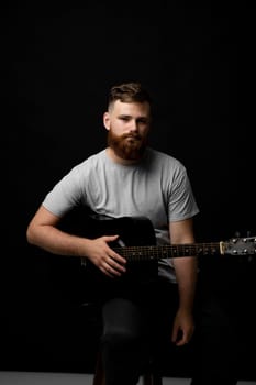 Bearded musician playing acoustic guitar in a dark room