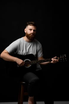 Portaraite of bearded musician man playing acoustic guitar in a dark room