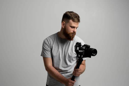 Side view of professional bearded videographer, cinematographer, cameraman using camera on gimbal stabilizer, steadicam on white background