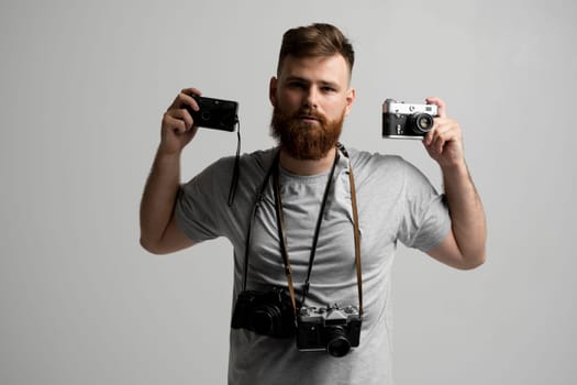 Professional bearded photographer holding a bunch of different vintage old cameras in a hands and on a shoulder