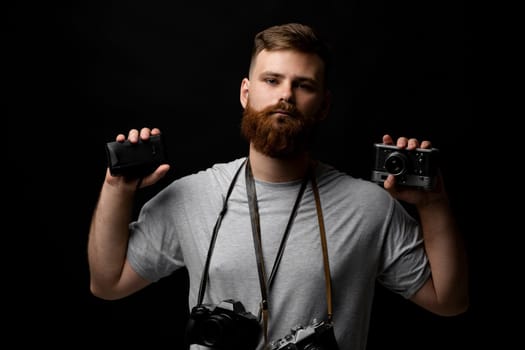 Professional bearded photographer holding a bunch of different vintage old cameras in a hands and on a shoulder