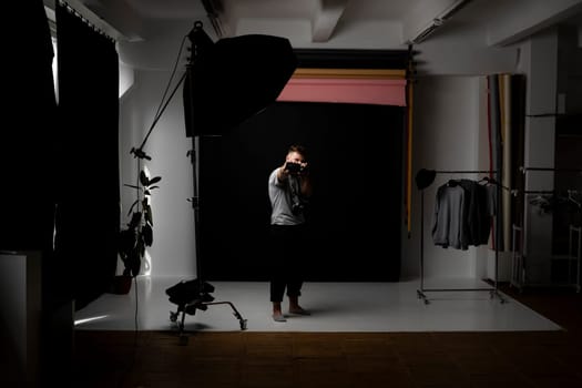 Handsome bearded photographer in a grey t-shirt with a bunch of different cameras in a hands and on a shoulder looking on a camera