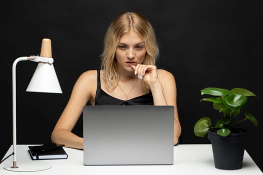 Portrait of attractive freelancer woman in a black t-shirt with a laptop in a studio with a black wall