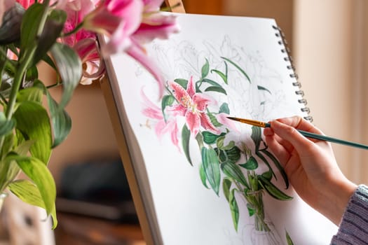 Young girl painting still life with flowers, purple lilies, with watercolor paints on the easel at home
