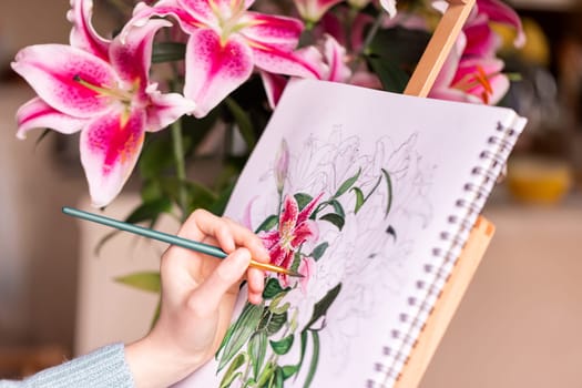 Young left-handed girl painting still life with flowers, purple lilies, with watercolor paints on the easel