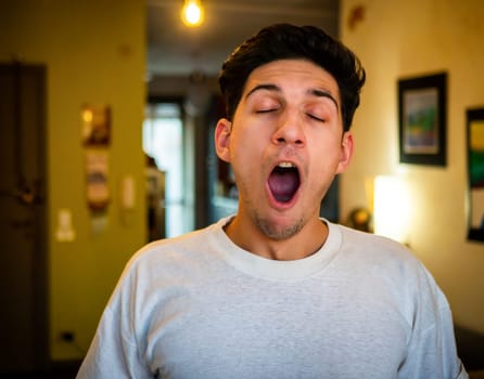 Young handsome man bored, yawning, standing at home in his living room