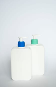 Two white cosmetic plastic bottle with pump dispenser pump and blue cap on white background. Liquid container for gel, lotion, cream, shampoo, bath foam