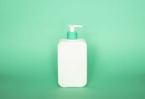 White bottle with a green dispenser for liquid soap, shampoo, gel on green background