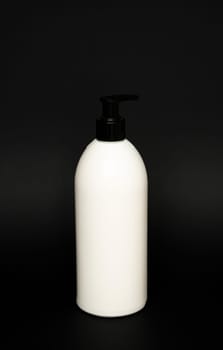 White unbranded bottle with a black dispenser isolated on black background. cosmetic packaging mockup with copy space. Bottle for a shower, gel, soap