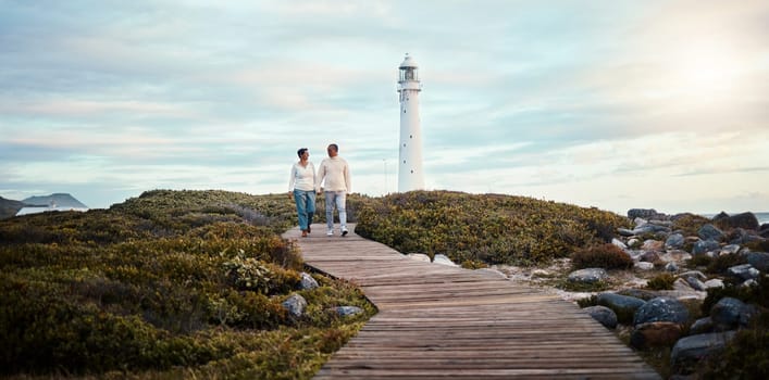 Romance, love and a couple holding hands while walking on the beach with a lighthouse in the background. Nature, view or blue sky mockup with a man and woman taking a romantic walk outside together.