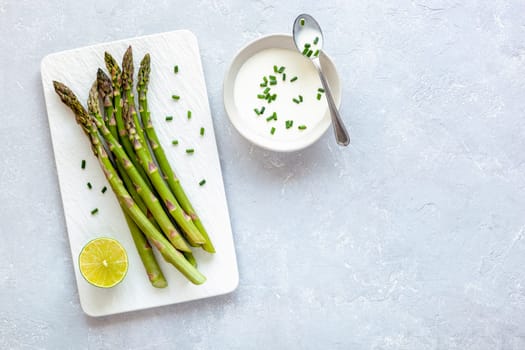 asparagus stems on the rectangular plate served with green cream and shrives, grey concrete background, top view, copyspace