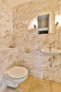 a small bathroom with marble walls and flooring, including a white toilet in the corner next to a sink