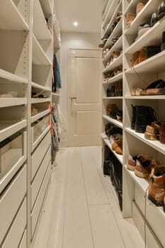 a walk - in closet with white shelvings and lots of shoes hanging on the wall next to it