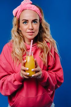 pregnant girl in pink clothes with a bottle of juice on a blue background.