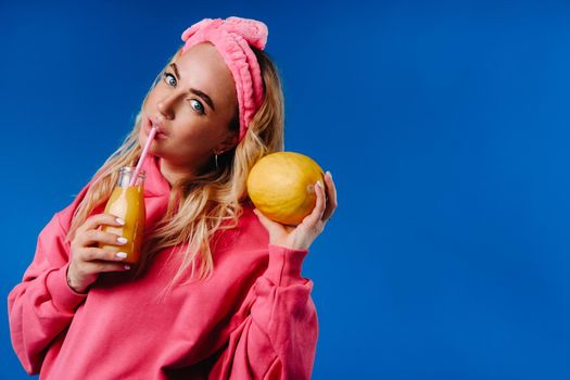 pregnant girl in pink clothes with a bottle of juice and a melon on a blue background.