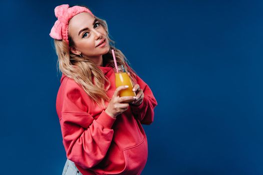 pregnant girl in pink clothes with a bottle of juice on a blue background.