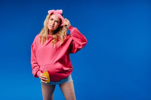 pregnant girl in pink clothes with a bottle of juice on a blue background.