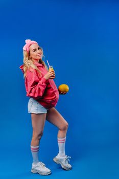 pregnant girl in pink clothes with a bottle of juice and a melon on a blue background.