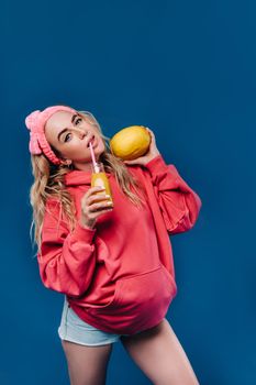 pregnant girl in pink clothes with a bottle of juice and a melon on a blue background.