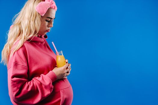pregnant girl in pink clothes with a bottle of juice on a blue background.