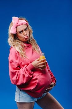 pregnant girl in pink clothes with a bottle of juice on a blue background.