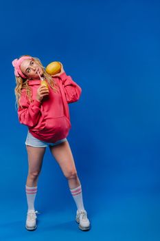 pregnant girl in pink clothes with a bottle of juice and a melon on a blue background.