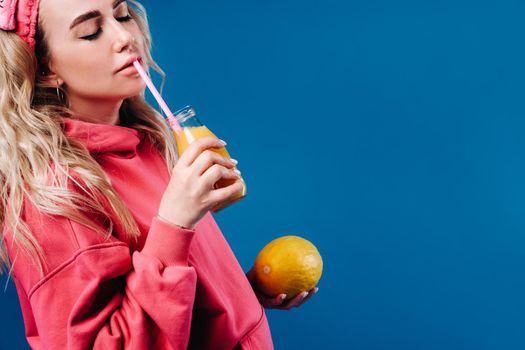 pregnant girl in pink clothes with a bottle of juice and a melon on a blue background.