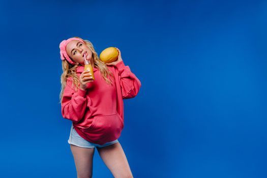pregnant girl in pink clothes with a bottle of juice and a melon on a blue background.