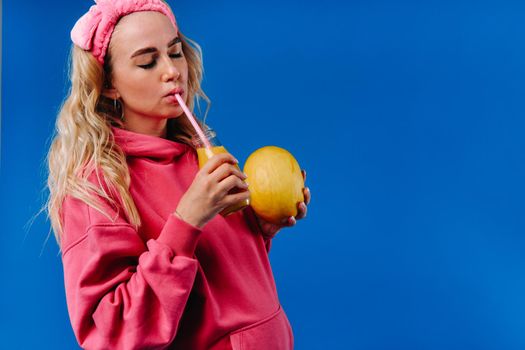pregnant girl in pink clothes with a bottle of juice and a melon on a blue background.